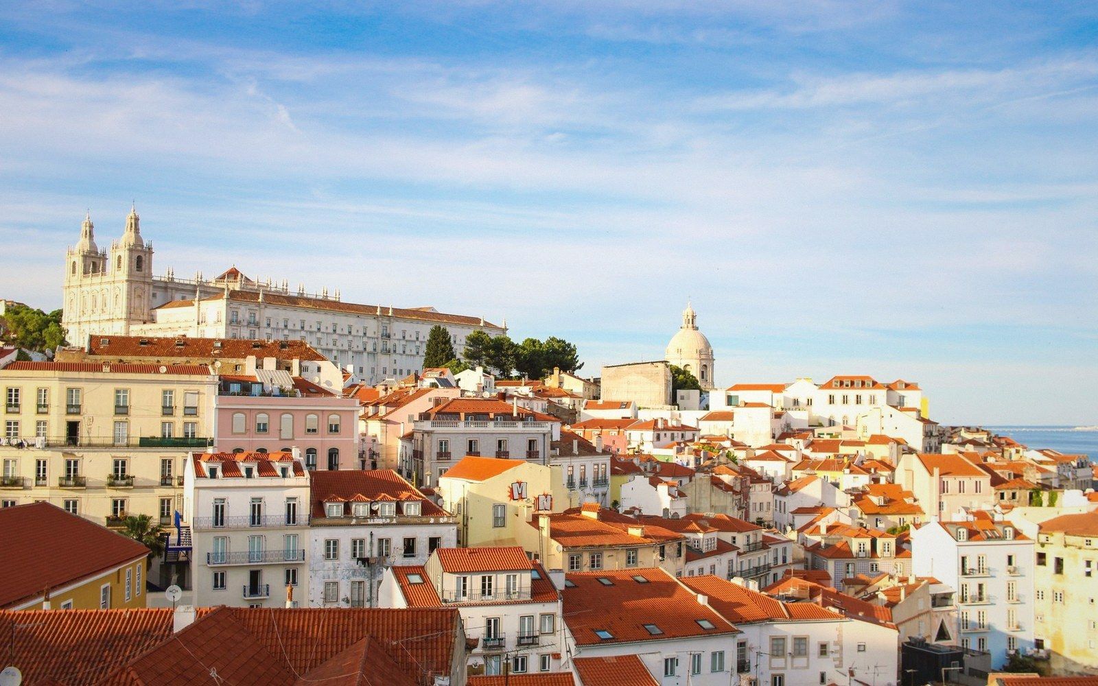 Red-tiled rooftops cascade over a hillside neighborhood with a domed church in the distance