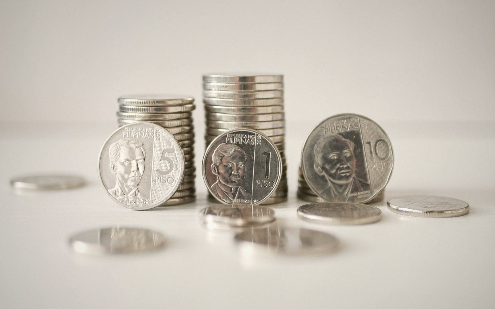 Stacked five, one, and ten peso coins from the Philippines standing upright on a white surface