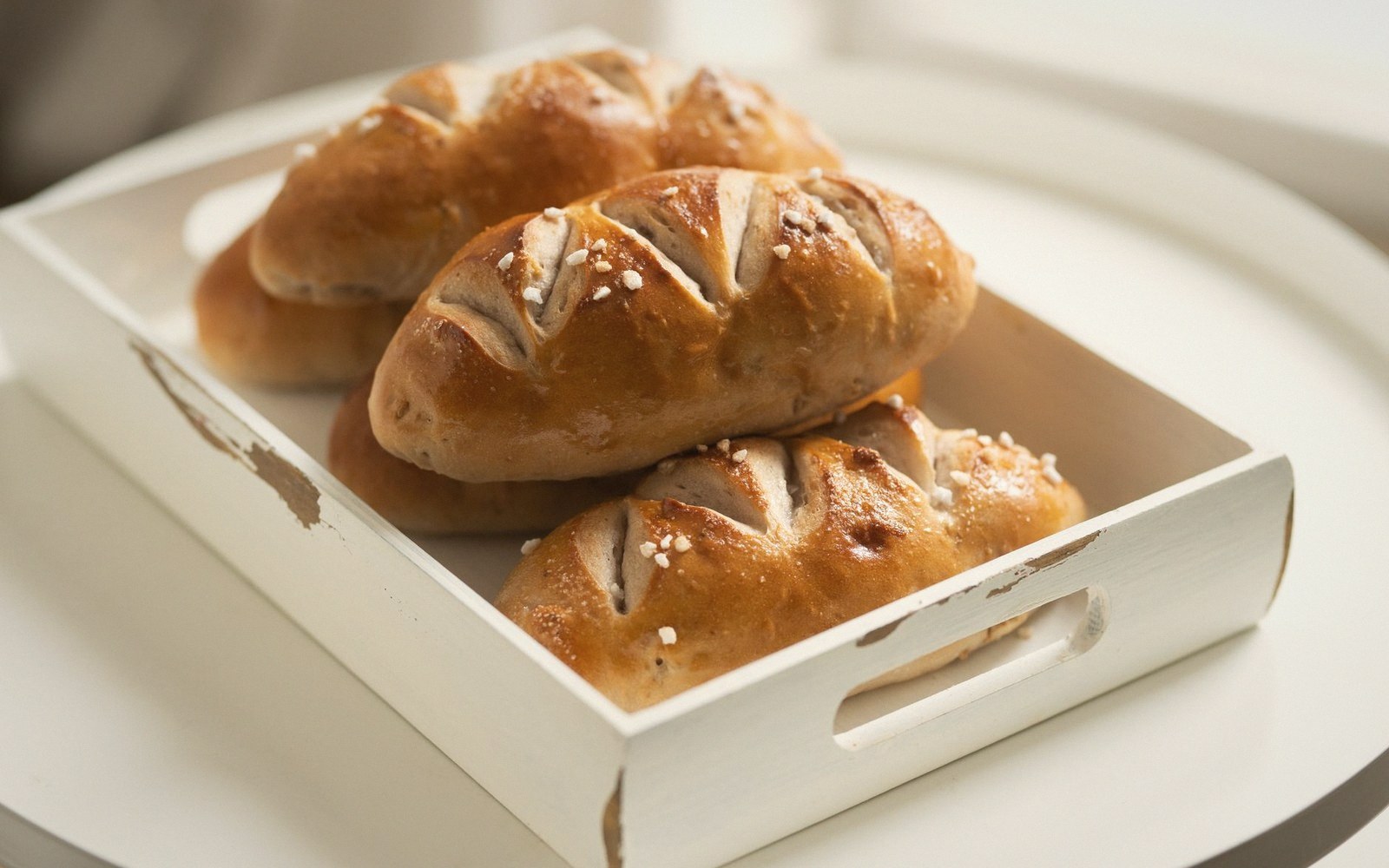 Freshly baked pretzel-style bread rolls with pearl sugar in a white wooden tray