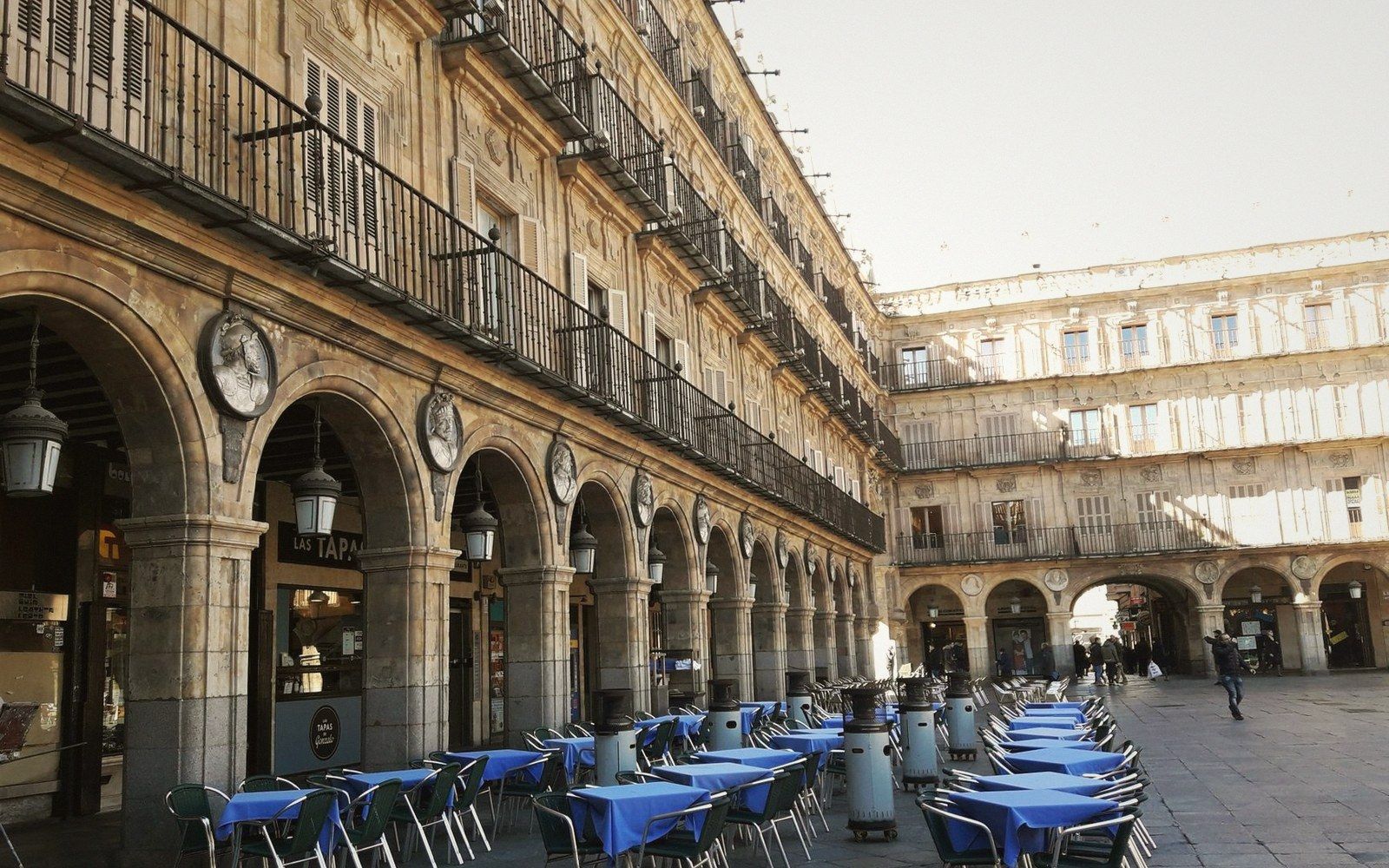 Arcaded facade of Plaza Mayor with rows of empty blue-clothed café tables below balconies