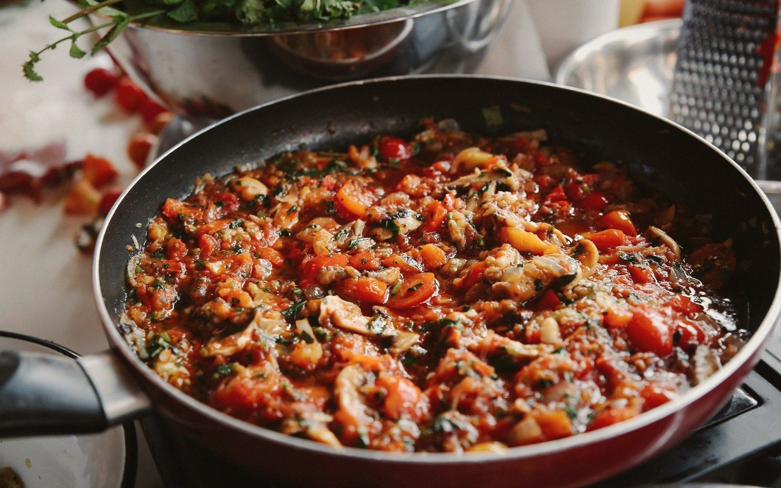 A skillet of simmering tomato sauce with mushrooms and herbs on the stove