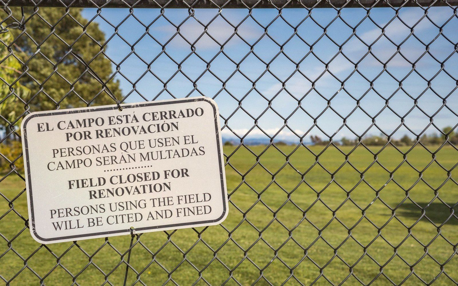 A bilingual sign on a chain-link fence warns that the field is closed for renovation