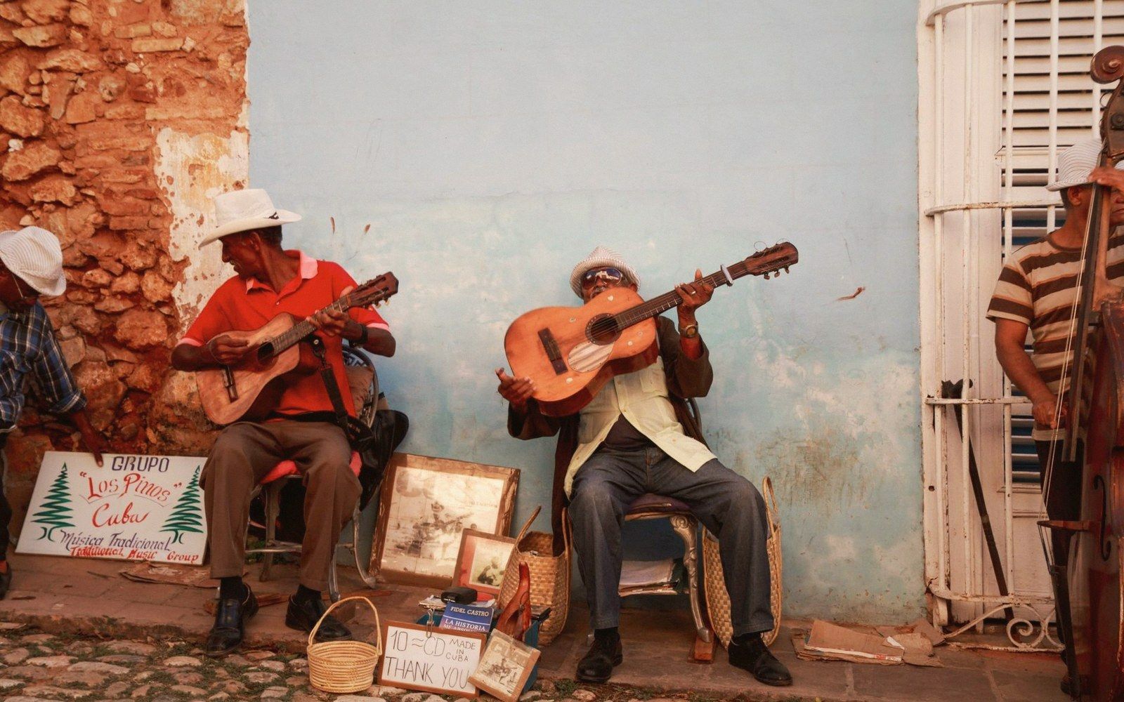 Street musicians play guitars beside a double bass against a weathered blue wall