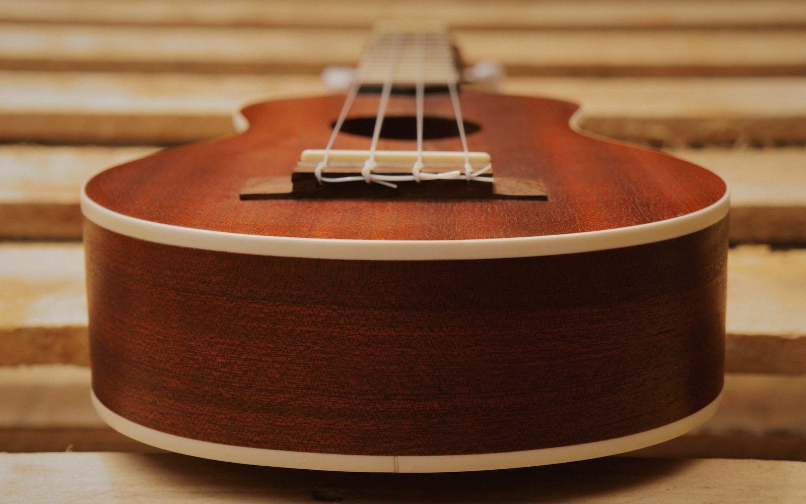 A classical guitar and a cavaquinho laid side by side on a wooden surface